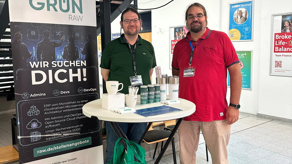 Zwei Mitarbeiter der GRÜN raw stehen am Messestand auf der FrOSCon 21.